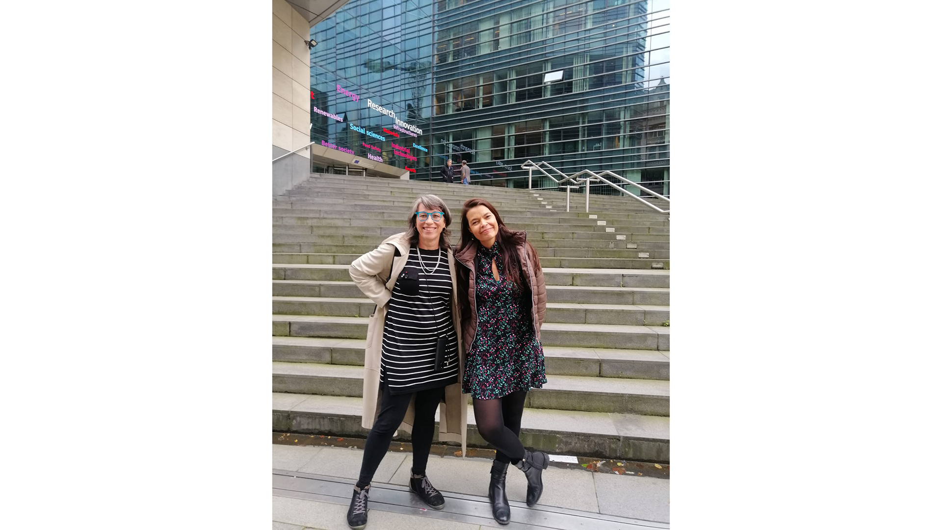 Two persons posing for the camera standing outside in front of a concrete stair case